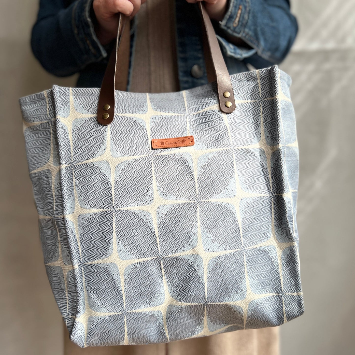 front view of blue and cream boxy tote with brown leather handles modelled by a lady to show size, handmade by Tallulah Riley