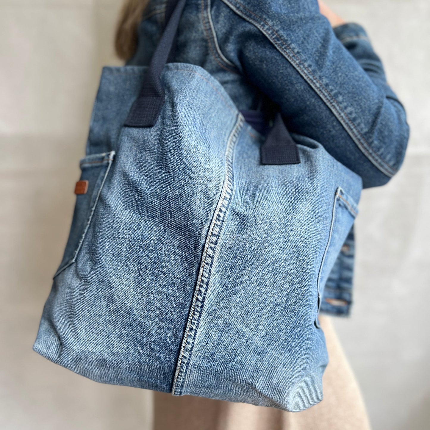 Modelled view of upcycled, re-used denim jeans tote bag with navy blue handles and two external pockets, handmade by Tallulah Riley