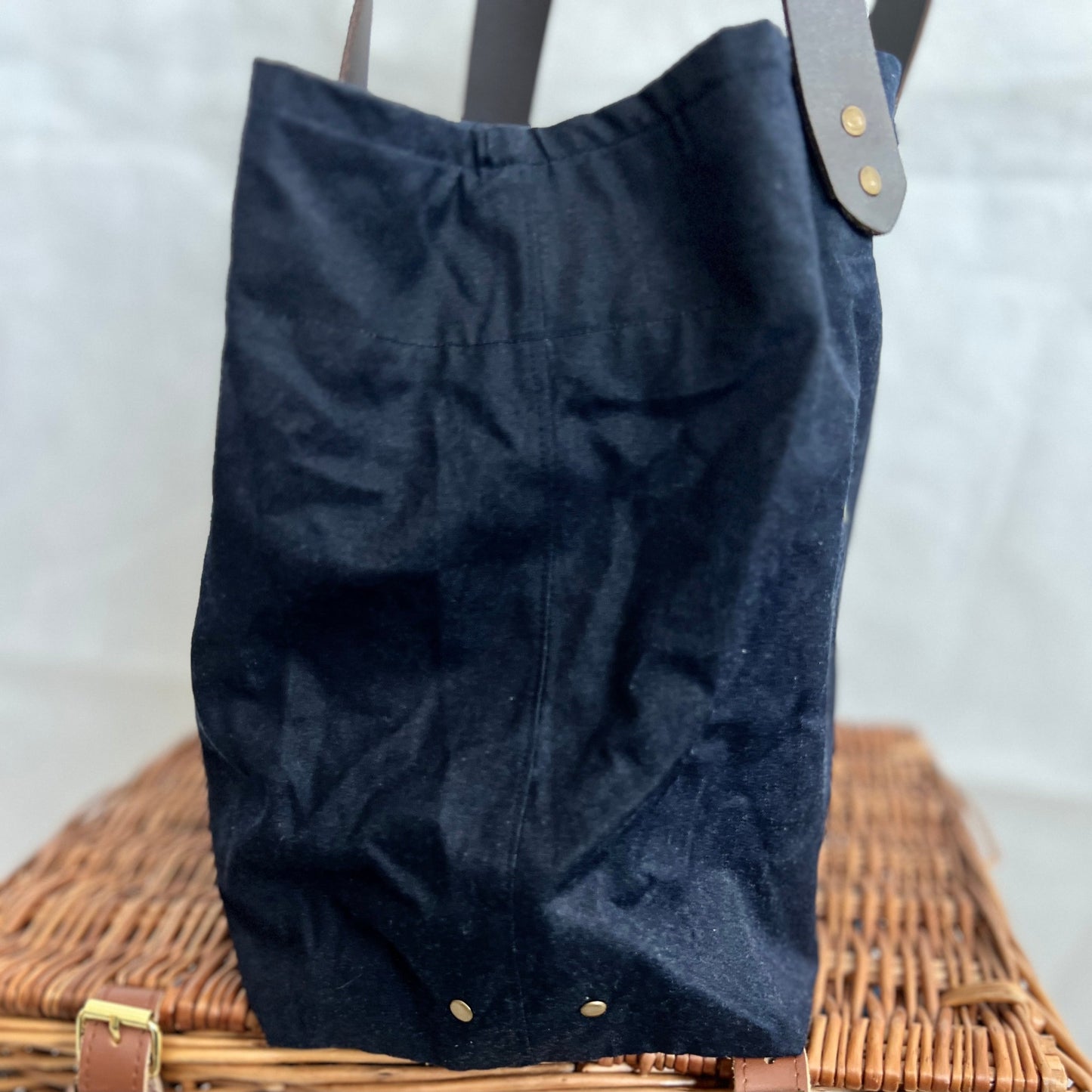 side view of navy blue waxed canvas tote bag with brown leather handles and antique brass stud detail, handmade by Tallulah Riley