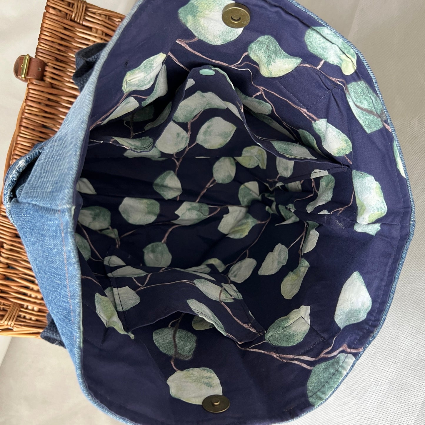 inside view of upcycled, re-used denim jeans tote bag with navy blue handles, contrasting lining with three internal pockets and antique brass magnetic closure, handmade by Tallulah Riley