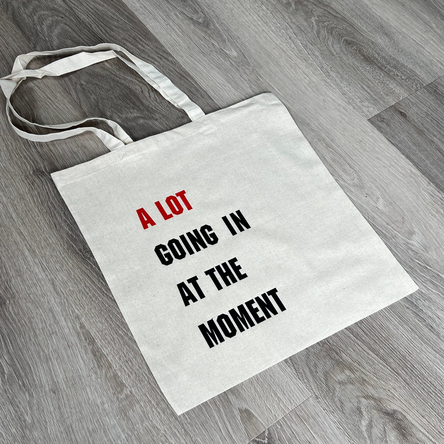 Natural tote bag with long handles, A Lot Going In At The Moment text to front in red and black, handmade by Tallulah Riley