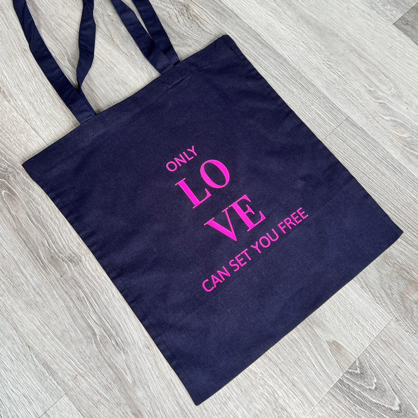 Navy blue text with the words 'only love can set you free' in fluorescent pink vinyl, handmade in Northamptonshire by Tallulah Riley