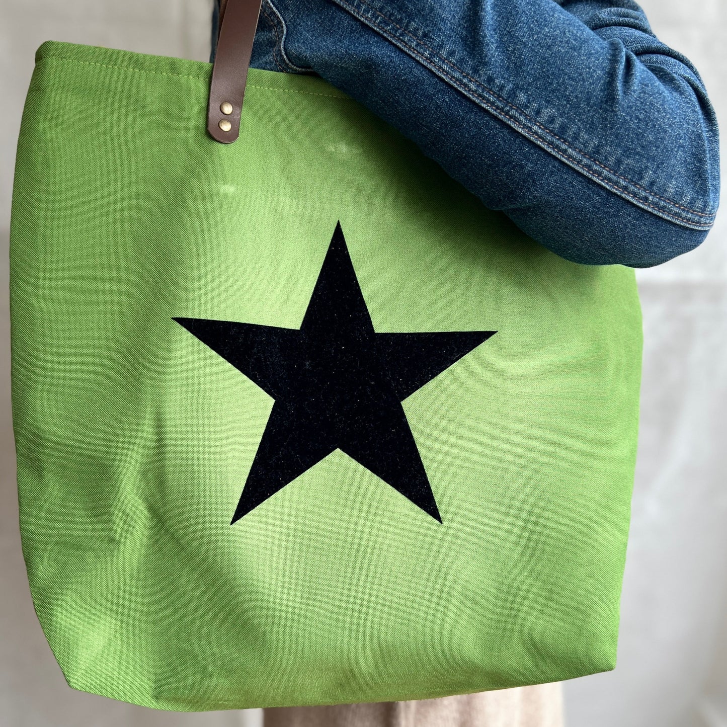 modelled view of bright green tote bag with navy blue star to front and brown leather handles, handmade by Tallulah Riley