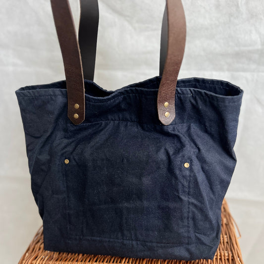 front view of navy blue waxed canvas tote bag with brown leather handles and antique brass stud detail, handmade by Tallulah Riley