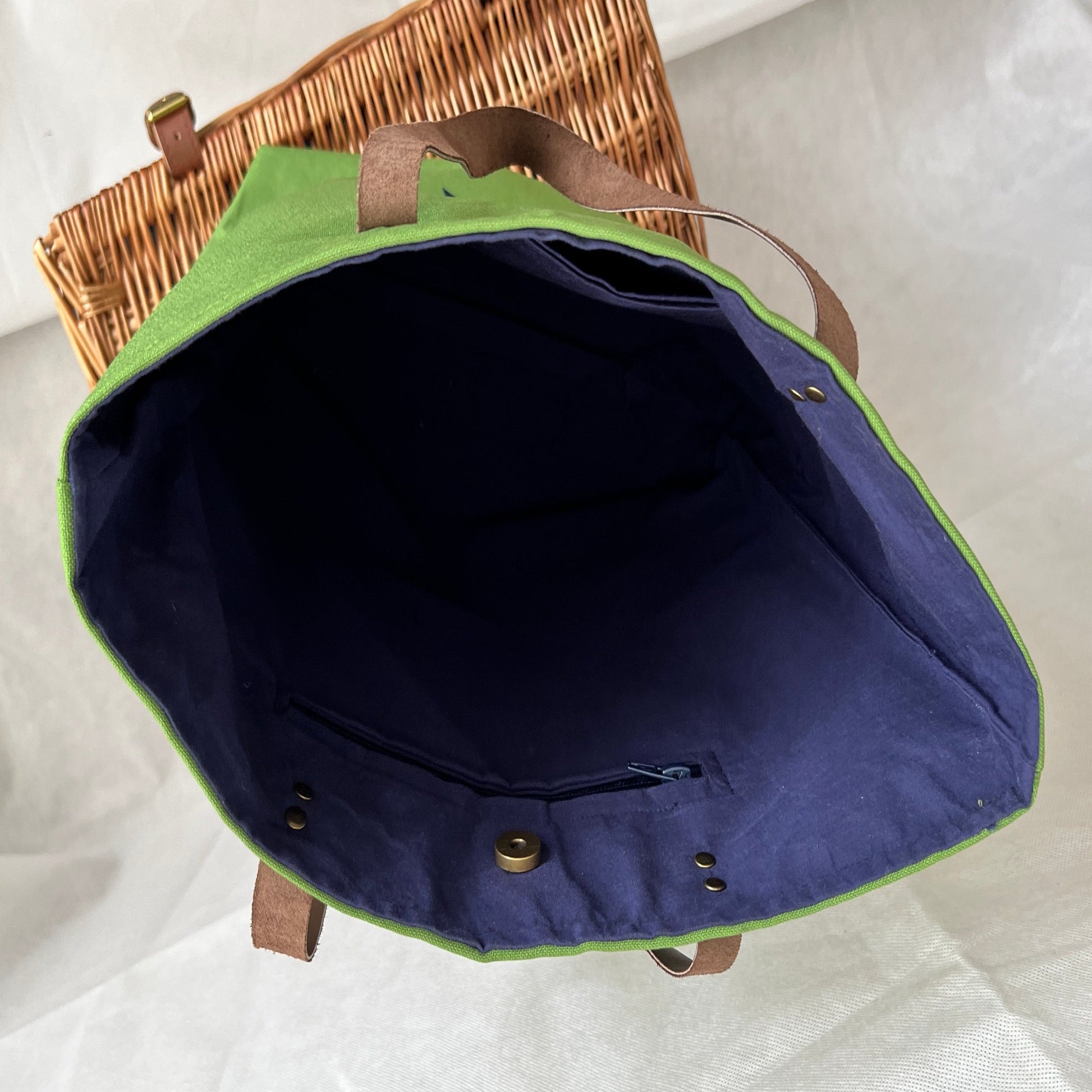 inside view of bright green tote bag, dark blue lining with one zipped and one open pocket, antique brass studs and magnetic closure, handmade by Tallulah Riley