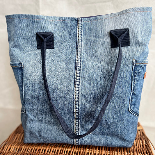 front view of upcycled, re-used denim jeans tote bag with side pockets and navy blue handles, handmade by Tallulah Riley