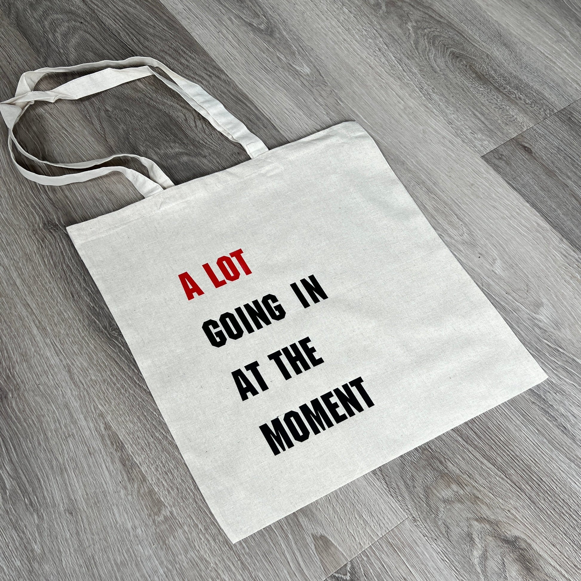 Natural tote bag with long handles, A Lot Going In At The Moment text to front in red and black, handmade by Tallulah Riley